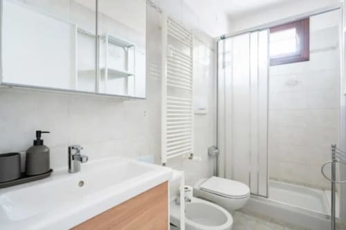 Modern bathroom with white vanity, mirror, toilet, bidet, and glass shower enclosure in Bealux Venice apartment