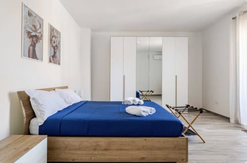 Camera da letto moderna con letto in legno, piumone blu, cuscini bianchi e armadio specchiato in appartamento a Brindisi