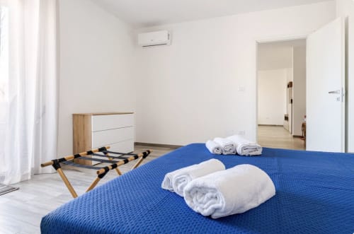 Camera moderna dell'appartamento Epico Brindisi con letto blu, biancheria bianca, cassettone in legno e aria condizionata