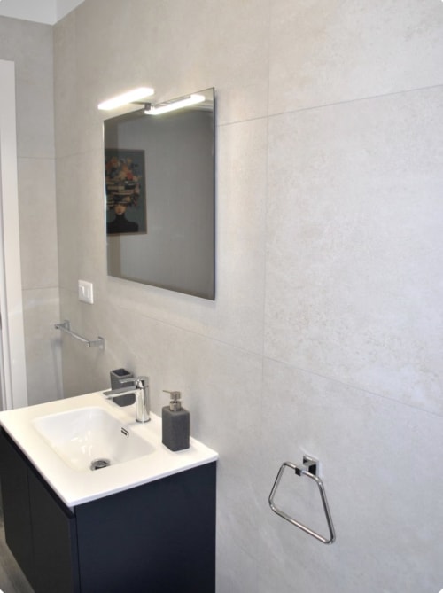 Moderno bagno di Brindisi Comfort House con lavabo bianco, mobile scuro, specchio illuminato e pareti in piastrelle chiare