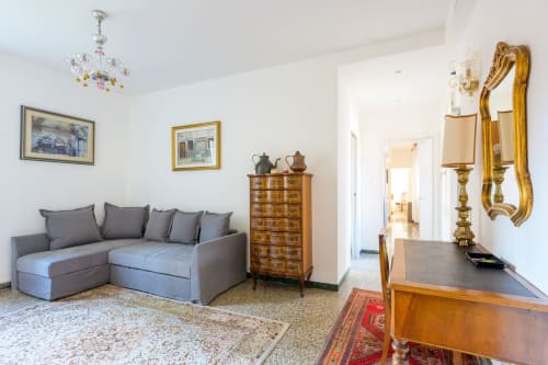 Elegant Venetian apartment living room with gray sofa, wooden furniture, gold mirror, and city views in Venice