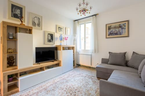 Lumineux séjour vénitien avec canapé gris, meuble TV en bois, écran, tableaux encadrés et vue sur la ville