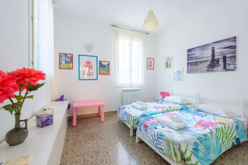 Chambre d'enfants lumineuse à l'appartement Bealux à Venise avec lits jumeaux, bureau rose, art mural coloré et fleurs rouges