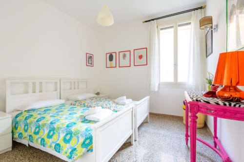 Chambre d'enfants lumineuse dans l'appartement de Venezia avec lits blancs, literie colorée et œuvres d'art encadrées en rouge
