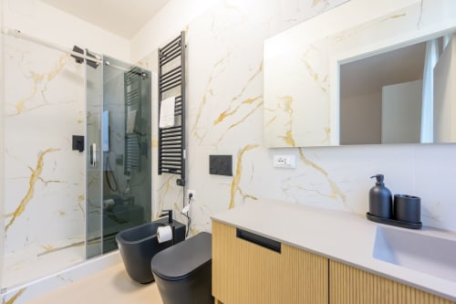 Salle de bain moderne en marbre dans l'appartement Bealux Venise avec douche vitrée, finitions noires et meuble vasque en bois