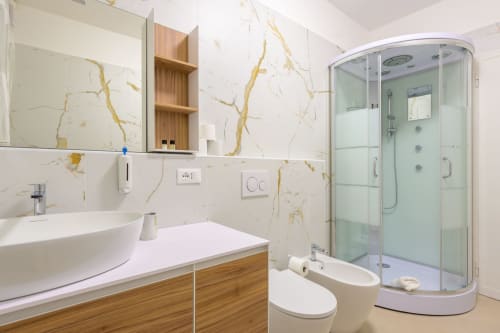 Salle de bain moderne et luxueuse à l'appartement Bealux à Venise avec murs en marbre, meuble-lavabo en bois et douche à effet pluie