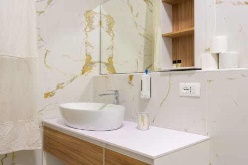 Salle de bain de luxe moderne dans l'appartement Bealux Venice avec murs en marbre, vasque blanche, meuble en bois et détails dorés