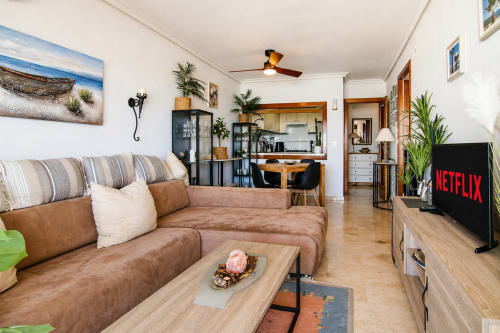 Sala de estar de la Marina Suite en Calpe con sofá de cuero marrón, mesa de centro de madera, TV y vista abierta a la cocina