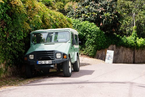 Vintage green Land Rover parked at Quinta dos Lobos Boutique Hotel entrance in Sintra, Portugal, surrounded by lush greenery.