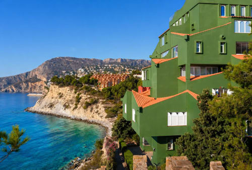 Bright green apartment building with terracotta balconies overlooking turquoise Mediterranean sea and dramatic cliffs in