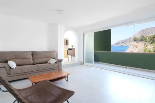 Modern living room at Riurau Home Calpe with gray sofa, wooden table, and sea view balcony overlooking Mediterranean cliffs