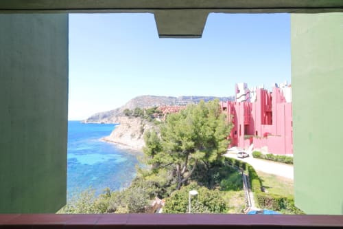Balcony view of Mediterranean coastline and cliff at Riurau Home apartment in Calpe, Spain with red building exterior