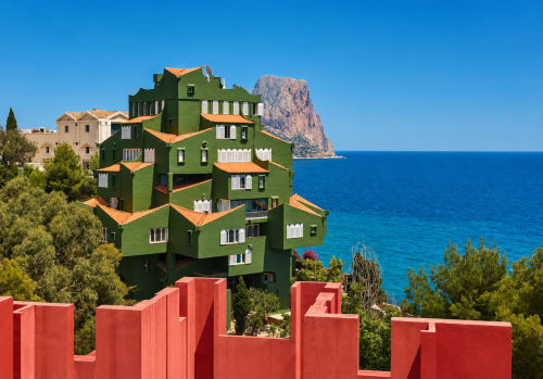 Green architectural building with orange roofs overlooking turquoise Mediterranean Sea and Peñón de Ifach rock in Calpe