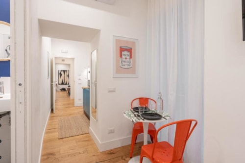 Modern dining area in Suite Maradona Naples B&B with red chairs, small table, and kitchen access through hallway