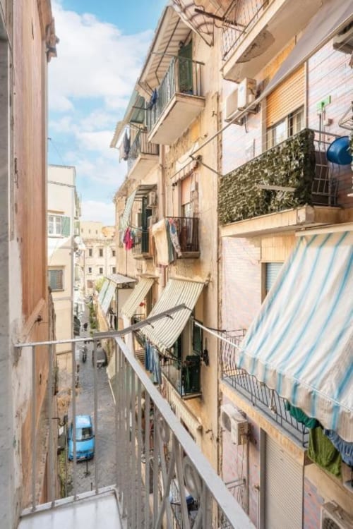 Narrow alley in Naples with colorful buildings, laundry hanging from balconies, and blue car parked below