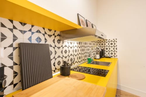 Modern kitchenette with bright yellow counter, geometric black and white backsplash tiles, and stainless steel sink at Suite