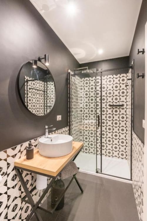 Modern bathroom in Suite Maradona Naples with black and white patterned tiles, round mirror, white vessel sink, and glass