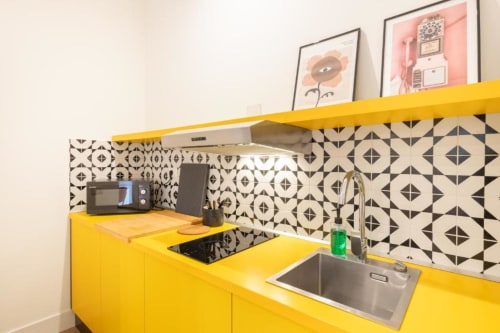Bright yellow kitchenette with geometric patterned backsplash, sink, cooktop, and appliances at Suite Maradona B&B in Naples