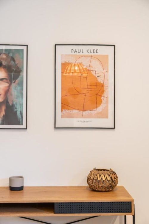 Minimalist room decor at Suite Maradona in Naples featuring Paul Klee artwork, wooden desk with ceramic cup and woven basket