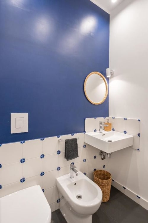 Modern bathroom at Suite Maradona Naples with blue walls, white sink, bidet, toilet, round mirror, and decorative