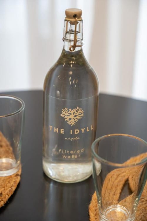 The Idylle filtered water bottle with glass at Suite Maradona Naples, displayed on dark table with amenities