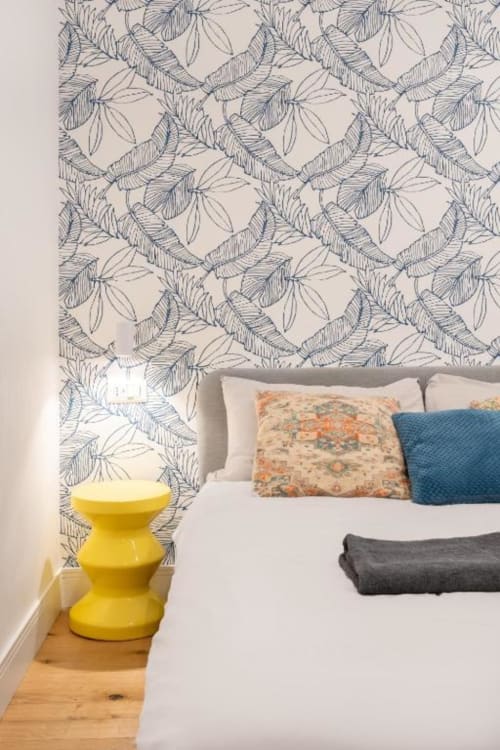 Modern bedroom at Suite Maradona Naples with botanical leaf wallpaper, bed with decorative pillows, and yellow side table