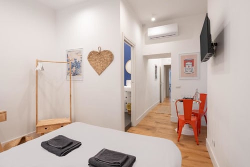 Modern Naples BnB double room with white walls, wooden bed, red chairs, and open-plan layout featuring kitchenette and living