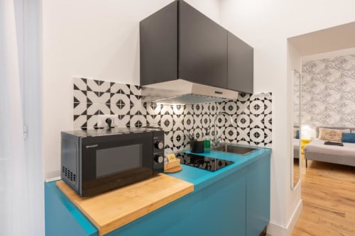 Modern kitchenette at Suite Maradona Naples with turquoise counters, geometric black-white tile backsplash, and microwave
