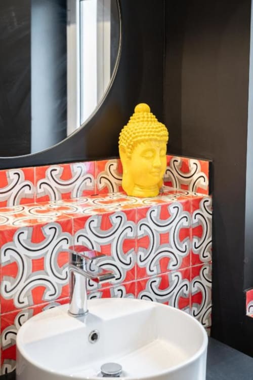 Yellow Buddha head decoration on red patterned tile backsplash above white sink in Suite Maradona Naples bathroom