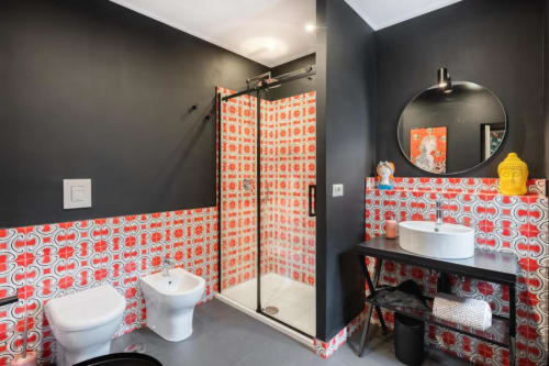 Modern bathroom at Suite Maradona Naples with red patterned tiles, dark walls, circular mirror, vessel sink, and walk-in