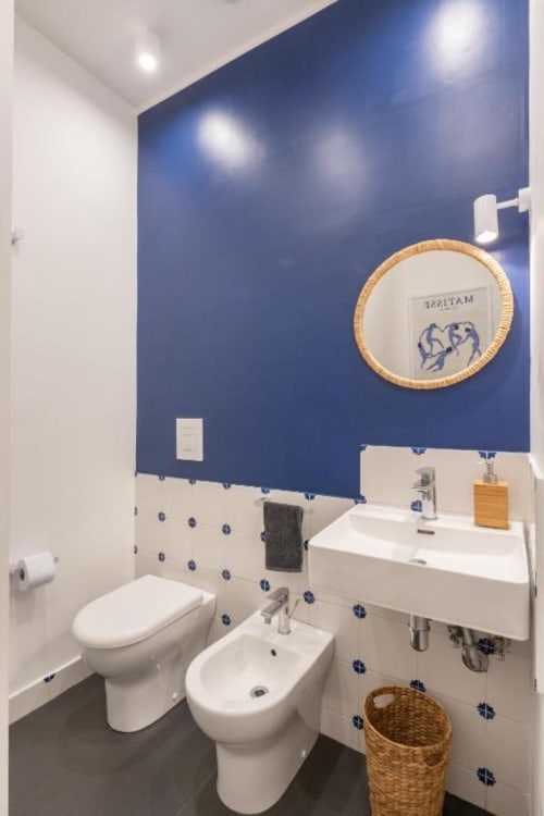 Modern bathroom at Suite Maradona Naples with blue accent wall, white fixtures, bidet, pedestal sink, and decorative circular