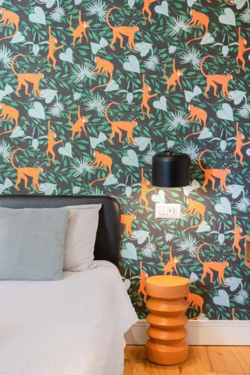 Suite Maradona bedroom with tropical wallpaper featuring orange monkeys and botanical motifs, orange side table and black