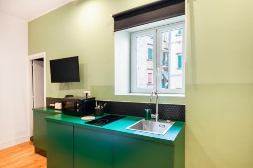 Modern green kitchenette in Suite Maradona Naples with sink, cooktop, and wall-mounted TV