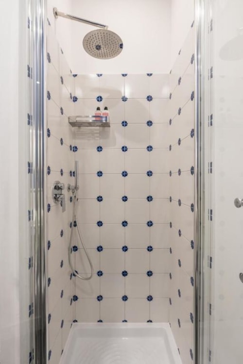 Modern shower stall with rainfall showerhead, handheld spray, and blue-accented tile pattern at Suite Maradona Naples