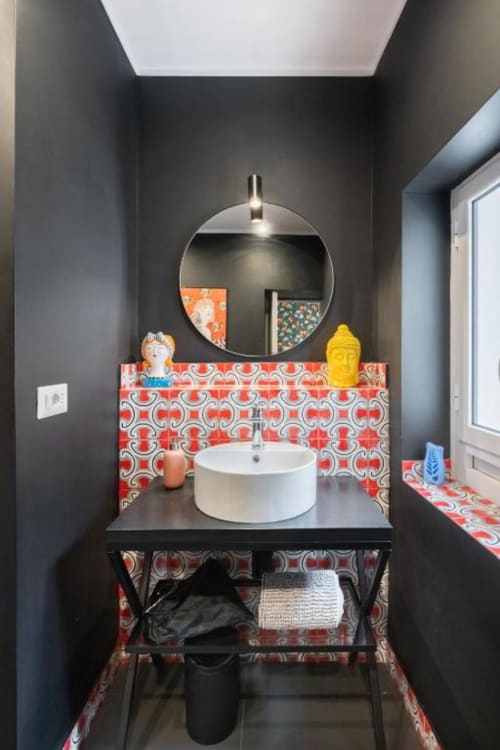 Modern bathroom vanity with circular mirror, white vessel sink, and red patterned tile backsplash at Suite Maradona Naples