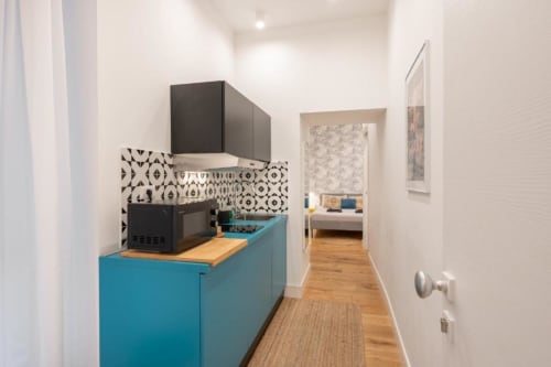 Modern kitchen galley with turquoise cabinetry, black appliances, patterned backsplash, wooden countertop at Suite Maradona