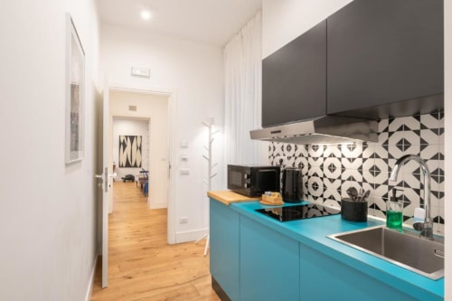 Modern kitchen at Suite Maradona Naples with turquoise cabinets, black stovetop, geometric backtile, stainless sink, and open