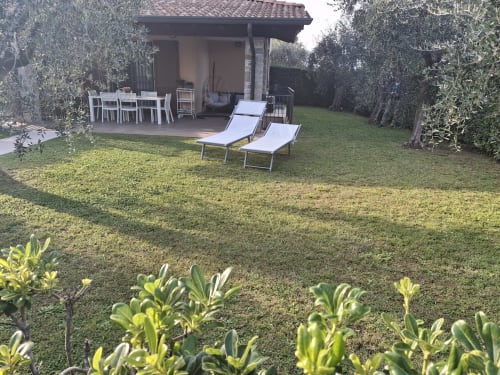 Giardino Prince Garda con lettini, zona pranzo, ulivi e prato curato a Serniga, Italia