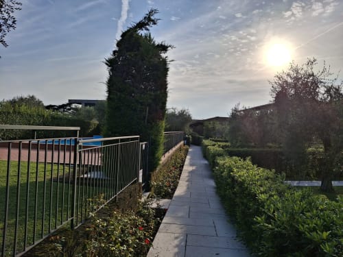 Suggestivo sentiero del giardino dell'hotel Prince Garda a Serniga con siepi, piscina azzurra e cielo soleggiato