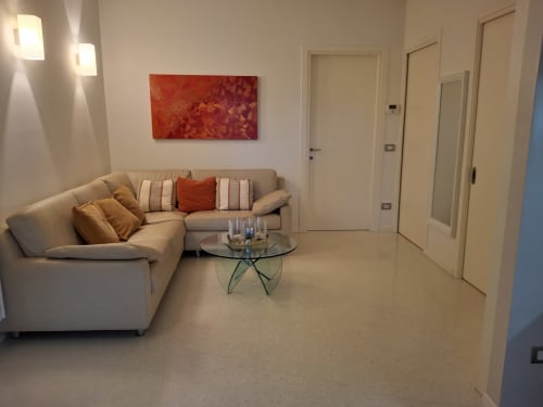 Moderna zona living dell'hotel Prince Garda a Serniga con divano beige, opera d'arte rossa e tavolino in vetro