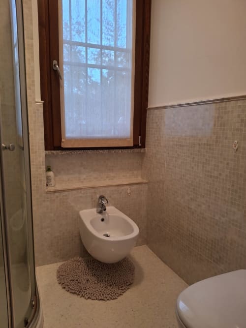 Bagno moderno con bidet, pareti piastrellate, finestra e pavimento riscaldato all'hotel Prince Garda di Serniga