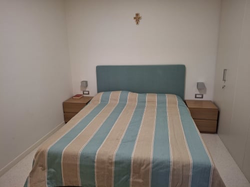 Camera da letto dell'hotel Prince Garda a Serniga con biancheria a righe, testata teal, comodini in legno e croce a muro
