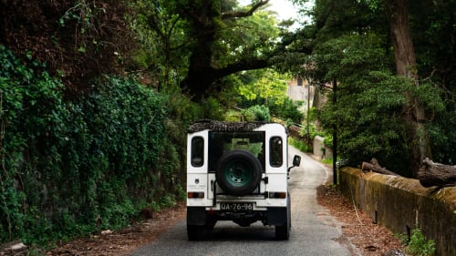 White Land Rover Defender driving through tree-lined forest road at Quinta dos Lobos Boutique Hotel in Sintra, Portugal