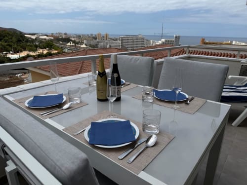 Rooftop dining setup in Costa Adeje with sea views, wine bottles, place settings with blue napkins overlooking Tenerife
