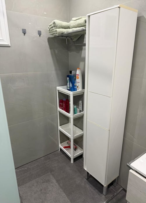 Modern shower room with tiled walls, white storage shelving holding toiletries and cream towels, at Costa Adeje apartment