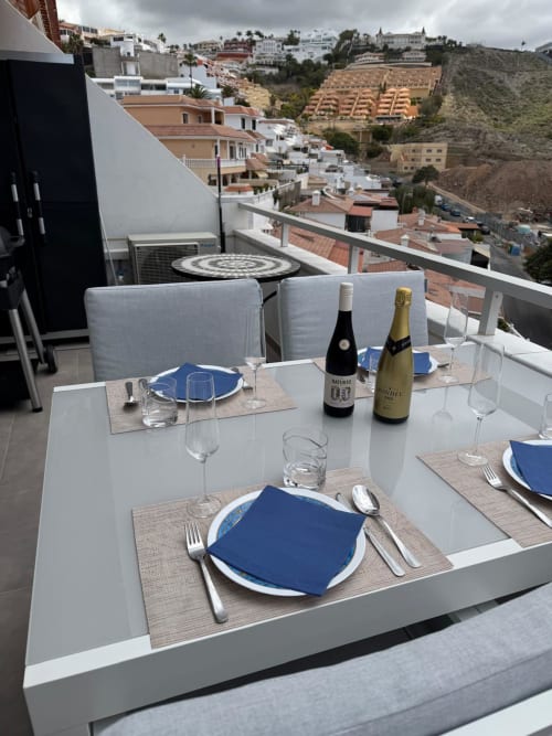 Elegant outdoor dining table set with wine bottles overlooking Costa Adeje hillside apartment buildings in Tenerife