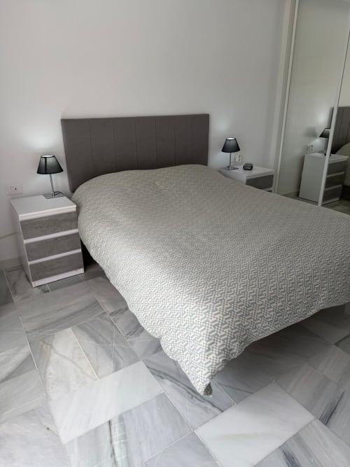 Modern bedroom in Costa Adeje apartment with dark headboard, patterned bedcover, white nightstands with lamps, and marble