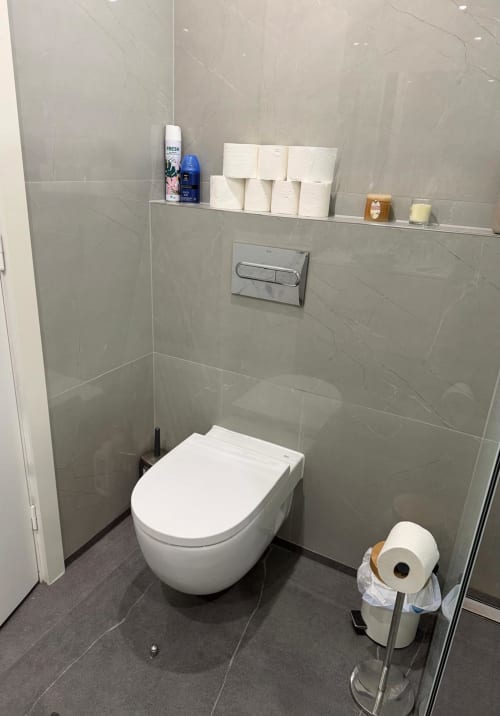 Modern bathroom in Costa Adeje apartment with wall-mounted toilet, gray tile, floating shelf with toiletries, and toilet