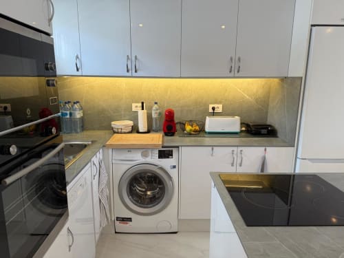 Modern kitchen in Costa Adeje apartment with white cabinets, gray countertops, washing machine, cooktop, and appliances