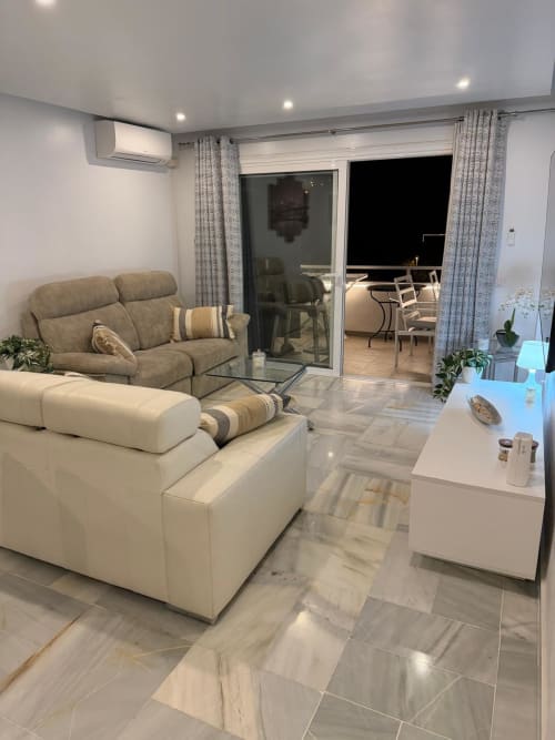 Modern living room in Costa Adeje apartment with beige sofa, white accent chair, marble flooring, and glass doors opening to